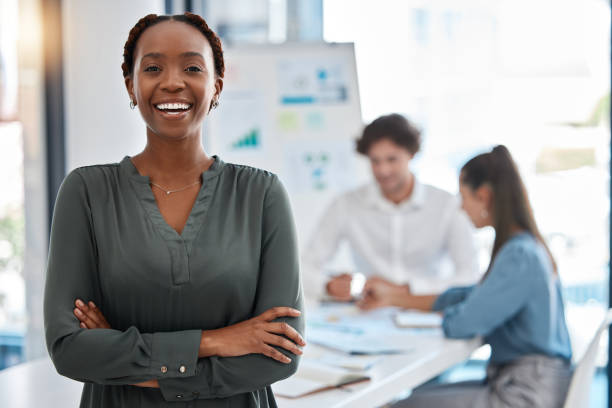 Portrait of a happy woman standing in a corporate office during a team analysis meeting. Black professional girl discussing and analyzing a project on a whiteboard in the company conference room.