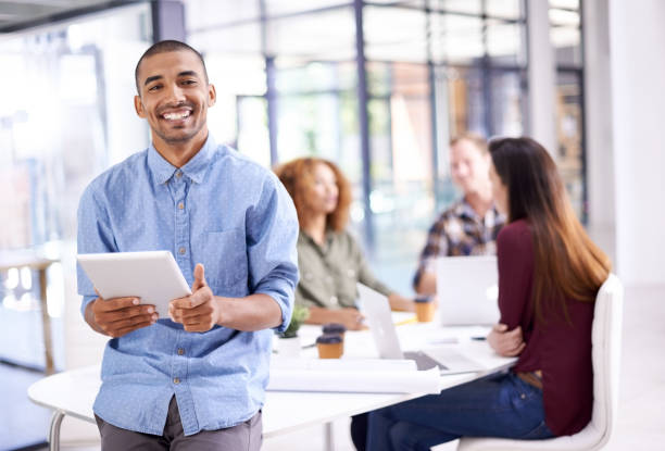 Portrait of a young designer working on a digital tablet with his colleagues in the background